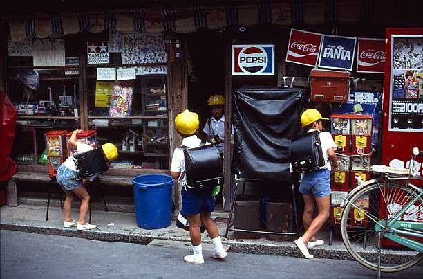 Three young Japanese schoolboys wearing yellow caps carrying large- Old Photo